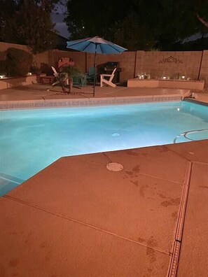 Ein Pool mit Fliesen umrandet, einem blauen Sonnenschirm und Gartenmöbeln.