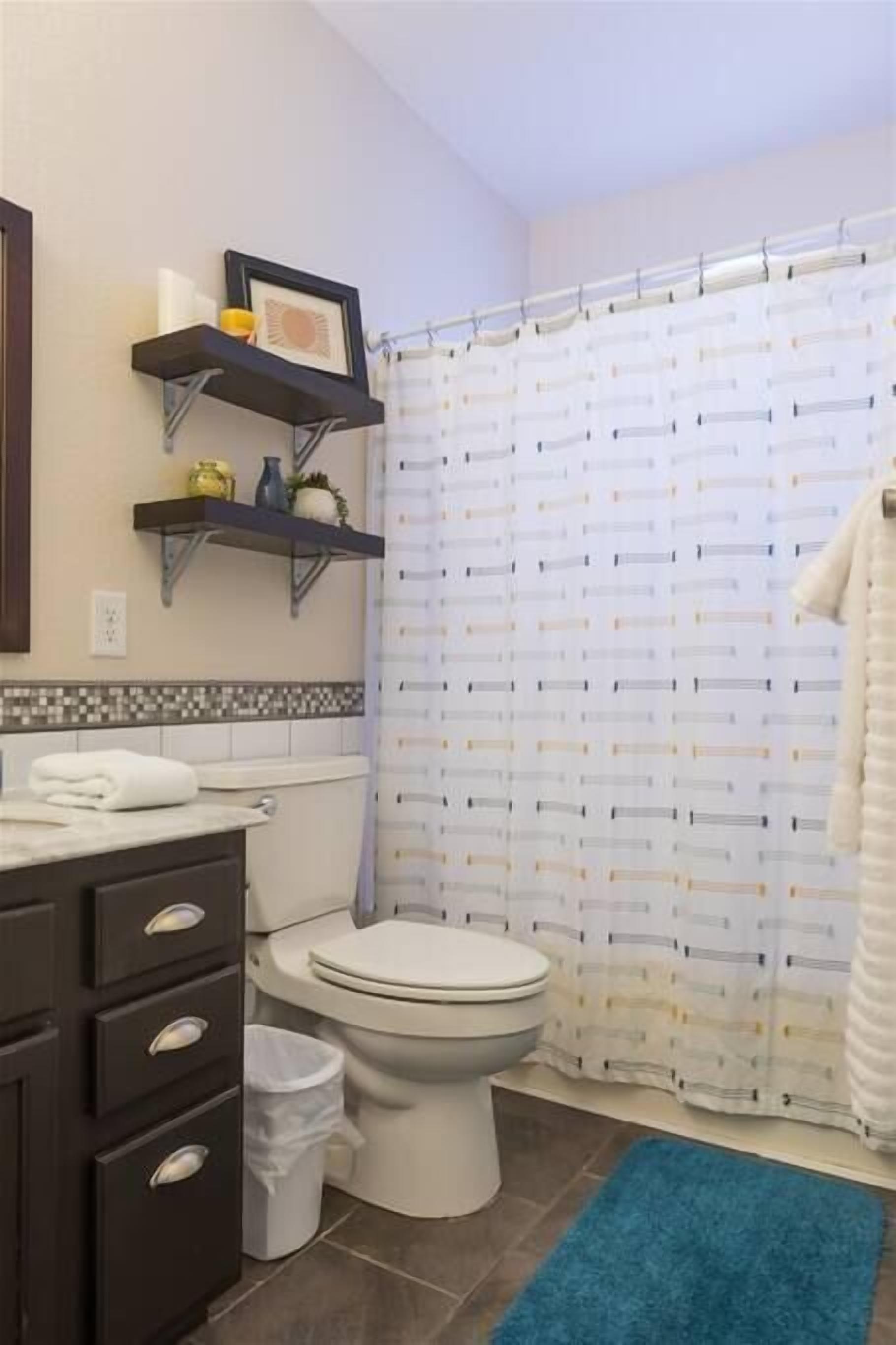 A bathroom with a toilet, a sink, a blue rug, and a shower curtain.