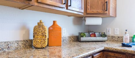 A kitchen with wooden cabinets, granite countertops, a spice rack, and a small plant.