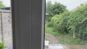 A door with a handle, a small potted plant, and a view of a garden with a wooden fence and greenery. - Immaculate 4 bedroom house,  Near central London (Edgware)