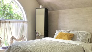Une chambre avec un grand lit, un ventilateur de plafond, une fenêtre avec des rideaux et une vue sur la verdure.