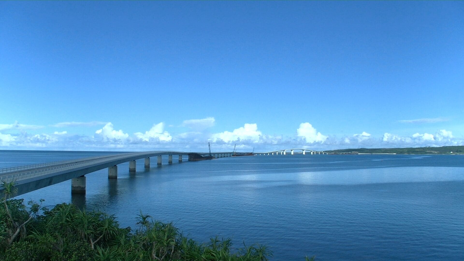 A long, curved bridge over calm water with a clear sky.
