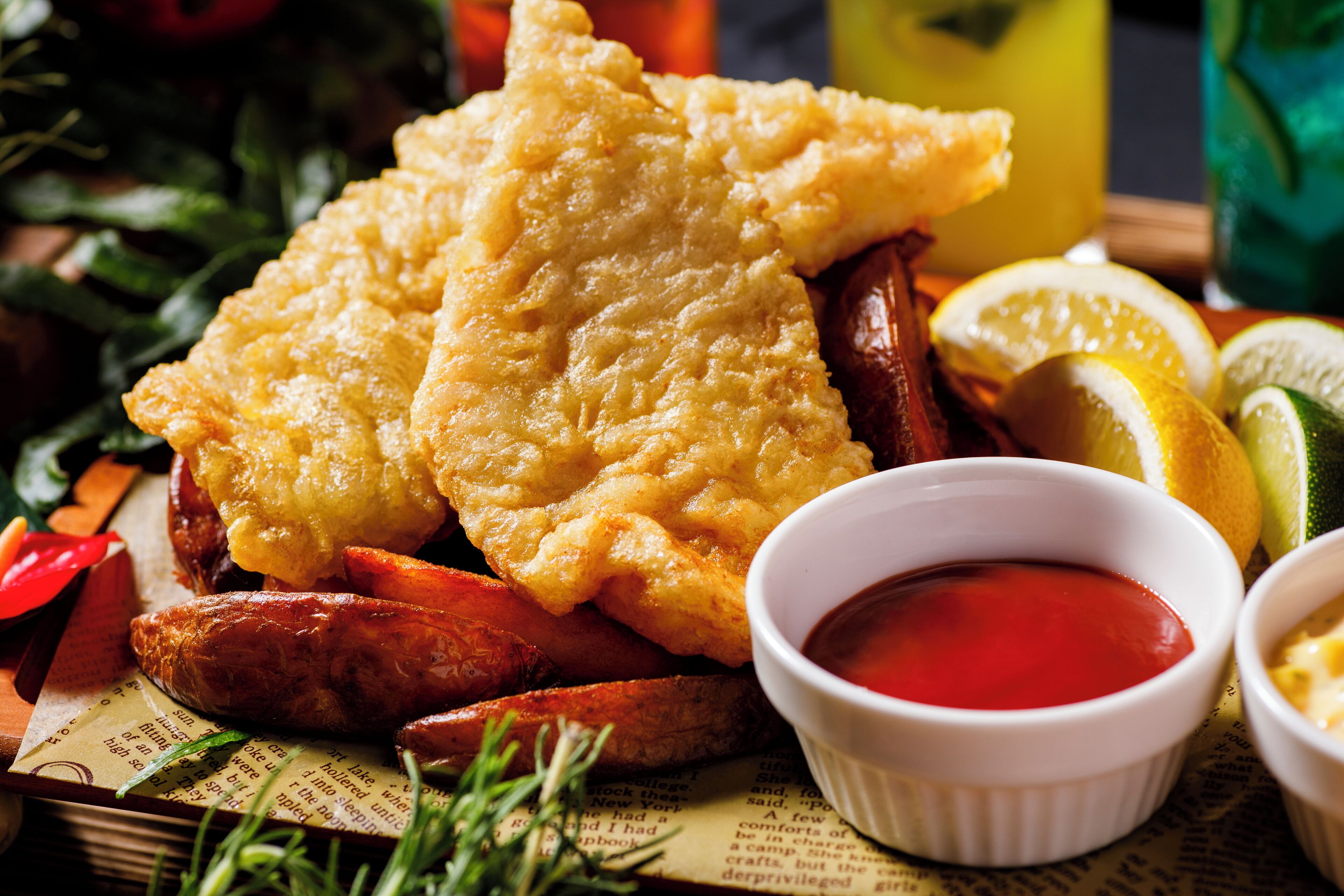 Un plato de pescado con patatas fritas acompañado de cuñas de patata, rodajas de limón y un pequeño recipiente de salsa.