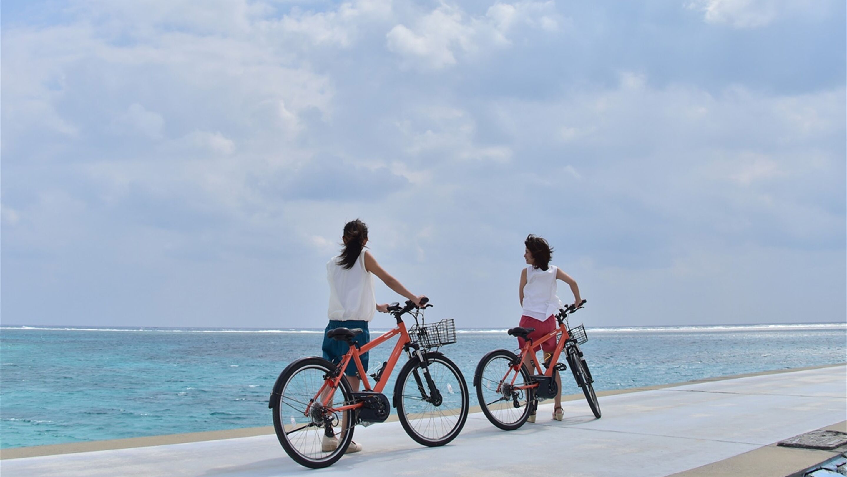 Duas pessoas andando de bicicleta em um caminho pavimentado à beira-mar.