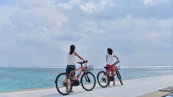 Duas pessoas andando de bicicleta em um caminho pavimentado à beira-mar.