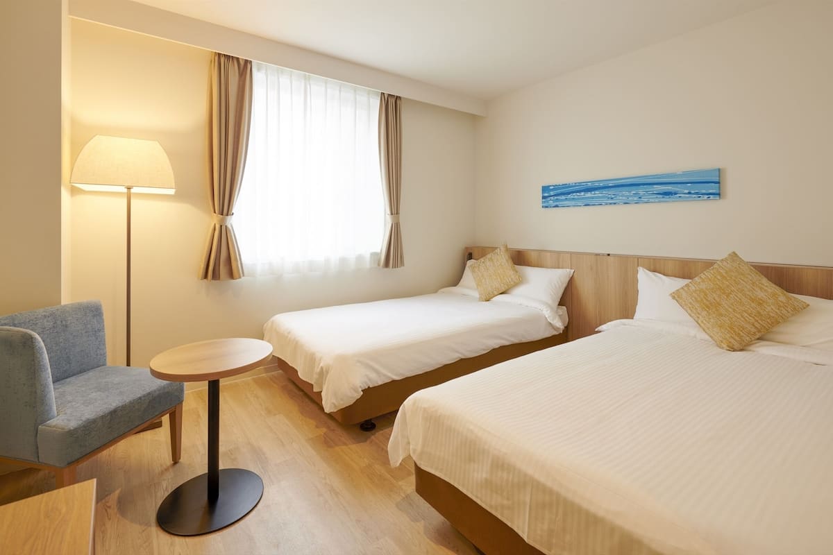 A hotel room with two single beds, a small round table, a sofa, and a TV.