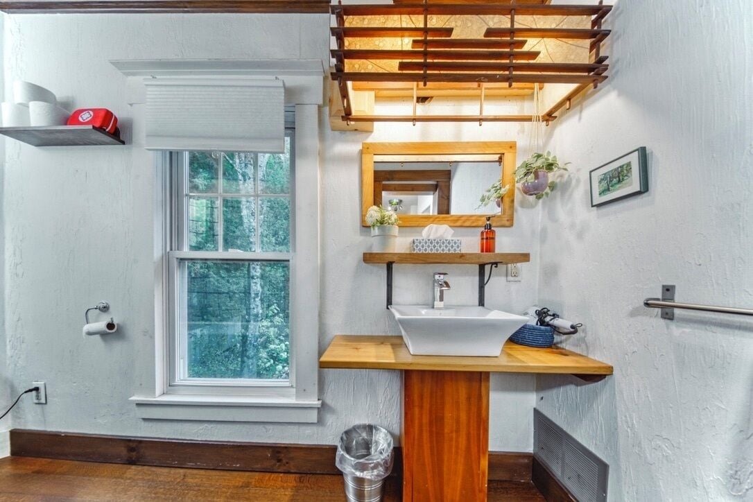A bathroom with a wooden vanity, a white sink, a mirror, a window, and a towel rack.