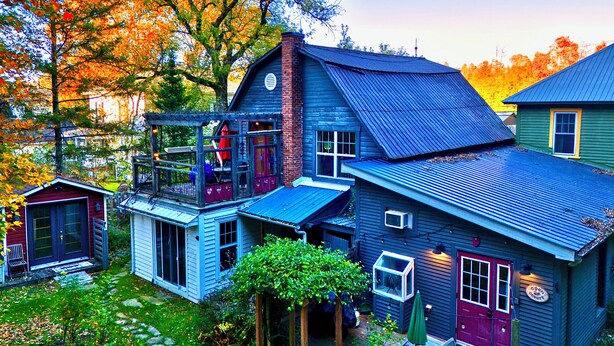 A rustic cabin with a porch, a small attached shed, and a garden area with a wooden deck. - Family Winter House in the ❤️ of the Eastern Townships (Ayer's Cliff)