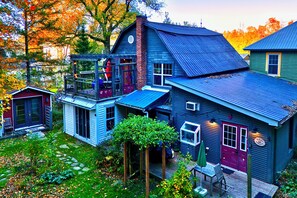 A rustic cabin with a porch, a small attached shed, and a garden area with a wooden deck. - Family Winter House in the ❤️ of the Eastern Townships (Ayer's Cliff)