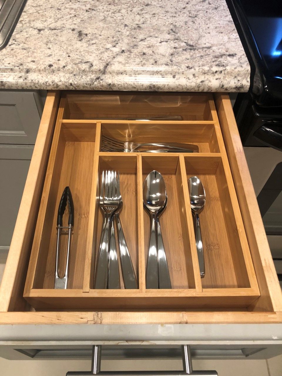 A drawer with a wooden interior containing a fork, knife, spoon, and spoon.