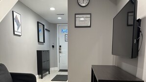 Ein Flur mit einem grauen Sofa, einer schwarzen Kommode, einer Uhr und einem gerahmten Zertifikat an der Wand.