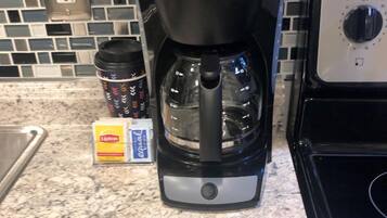 Una macchina da caffè Mr. Coffee su un piano di lavoro della cucina, con uno schienale piastrellato e un fornello.