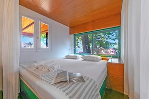 Un dormitorio con cama, almohadas, ventana y vistas al exterior.