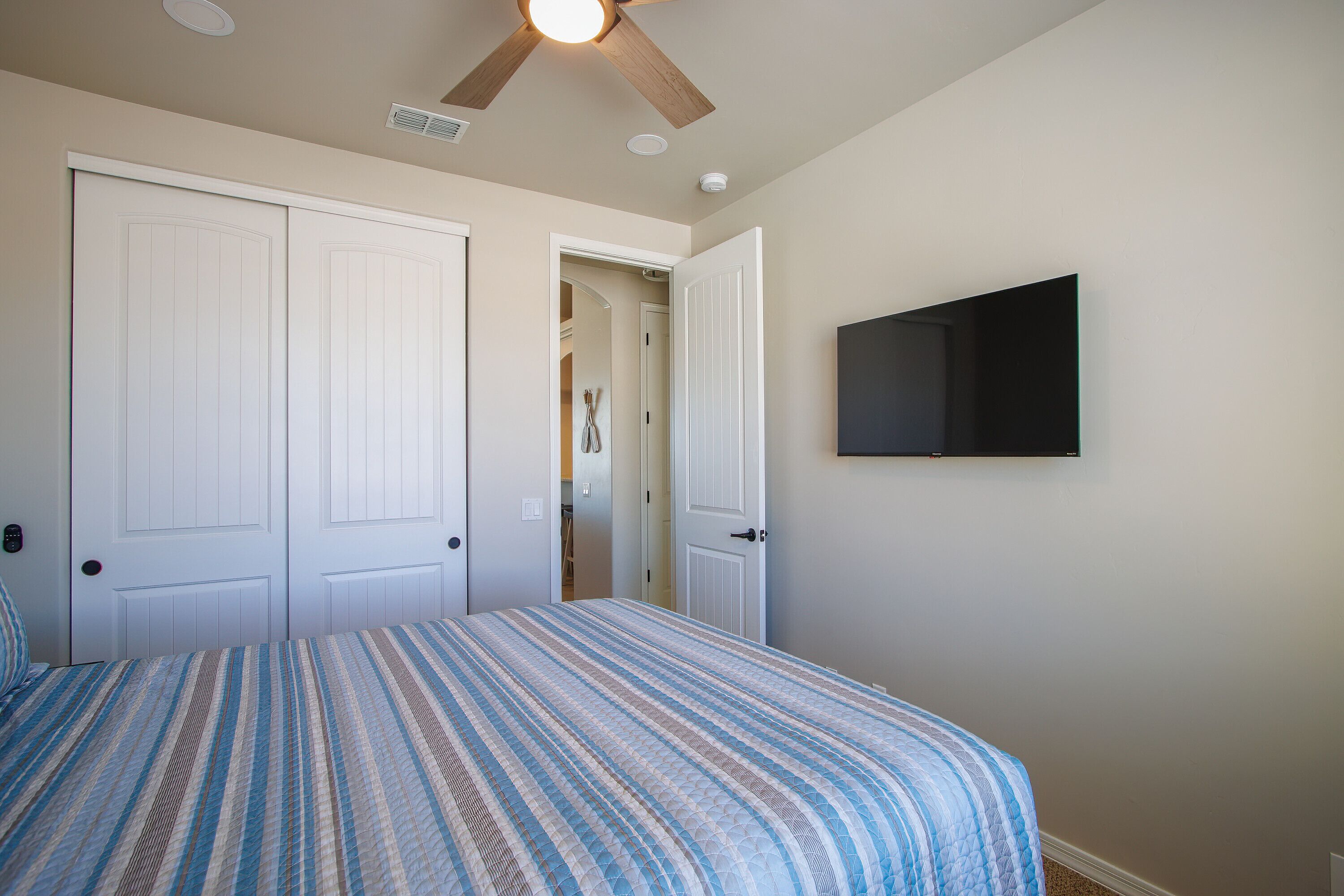 Un dormitorio con cama, ventilador de techo y televisor montado en la pared.