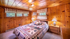 Un dormitorio de cabaña de madera con una cama grande, dos lámparas de noche y un ventanal con cortinas.