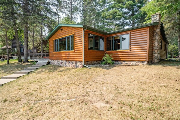 A log cabin with a stone foundation, large windows, and a stone chimney.