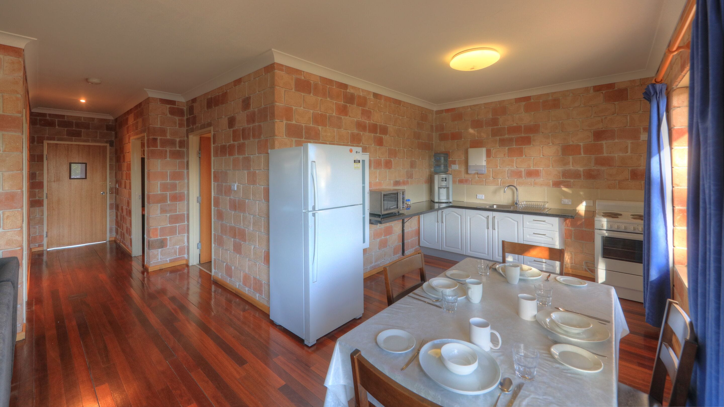 Cocina compacta con refrigerador, microondas y estufa. Se observa una mesa de comedor con platos y vasos.