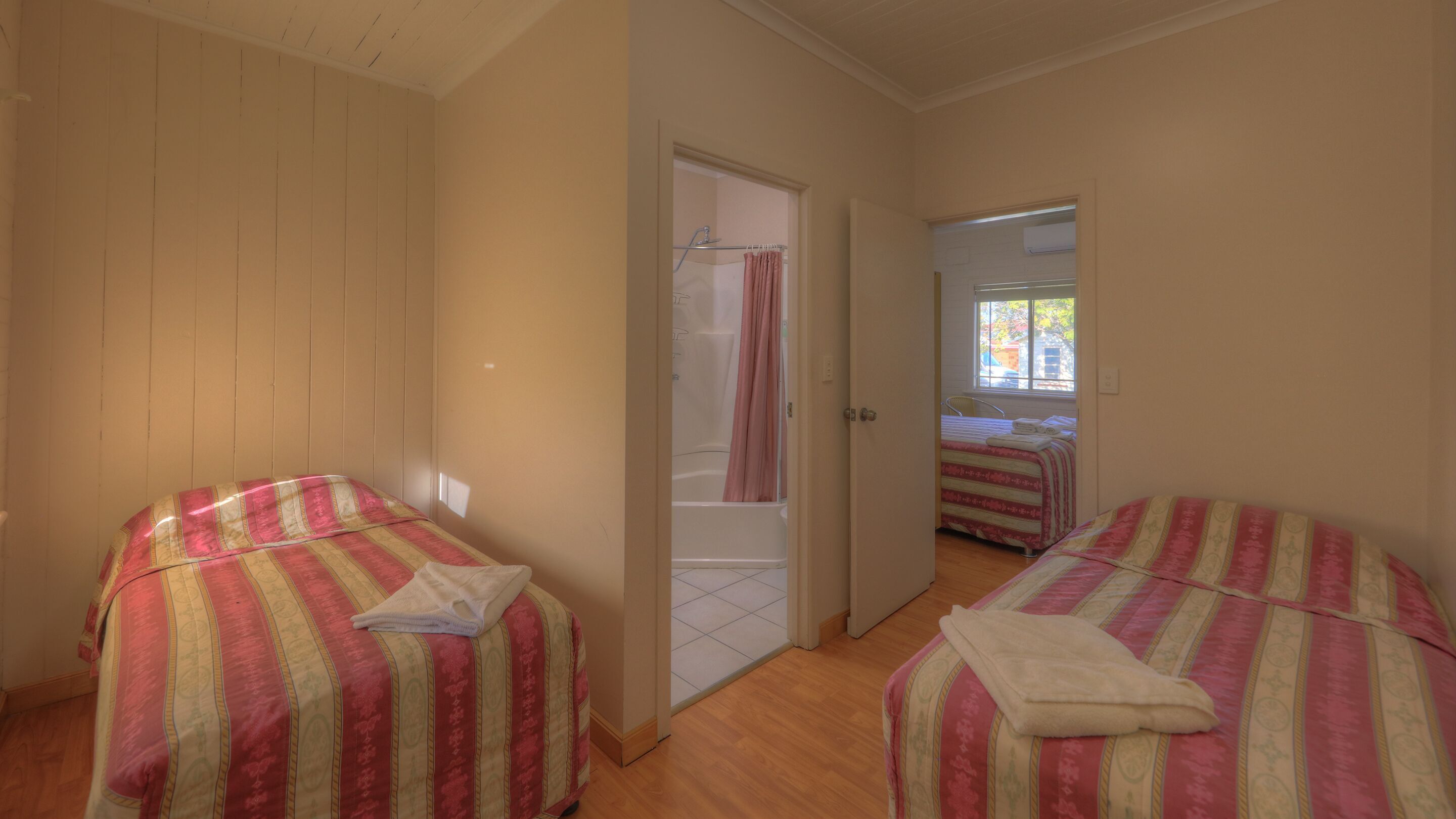 Una habitación con dos camas, un baño con ducha y ventana con vistas.