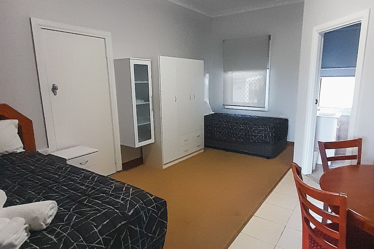 A bedroom with a bed, a wardrobe, a desk, and a chair.