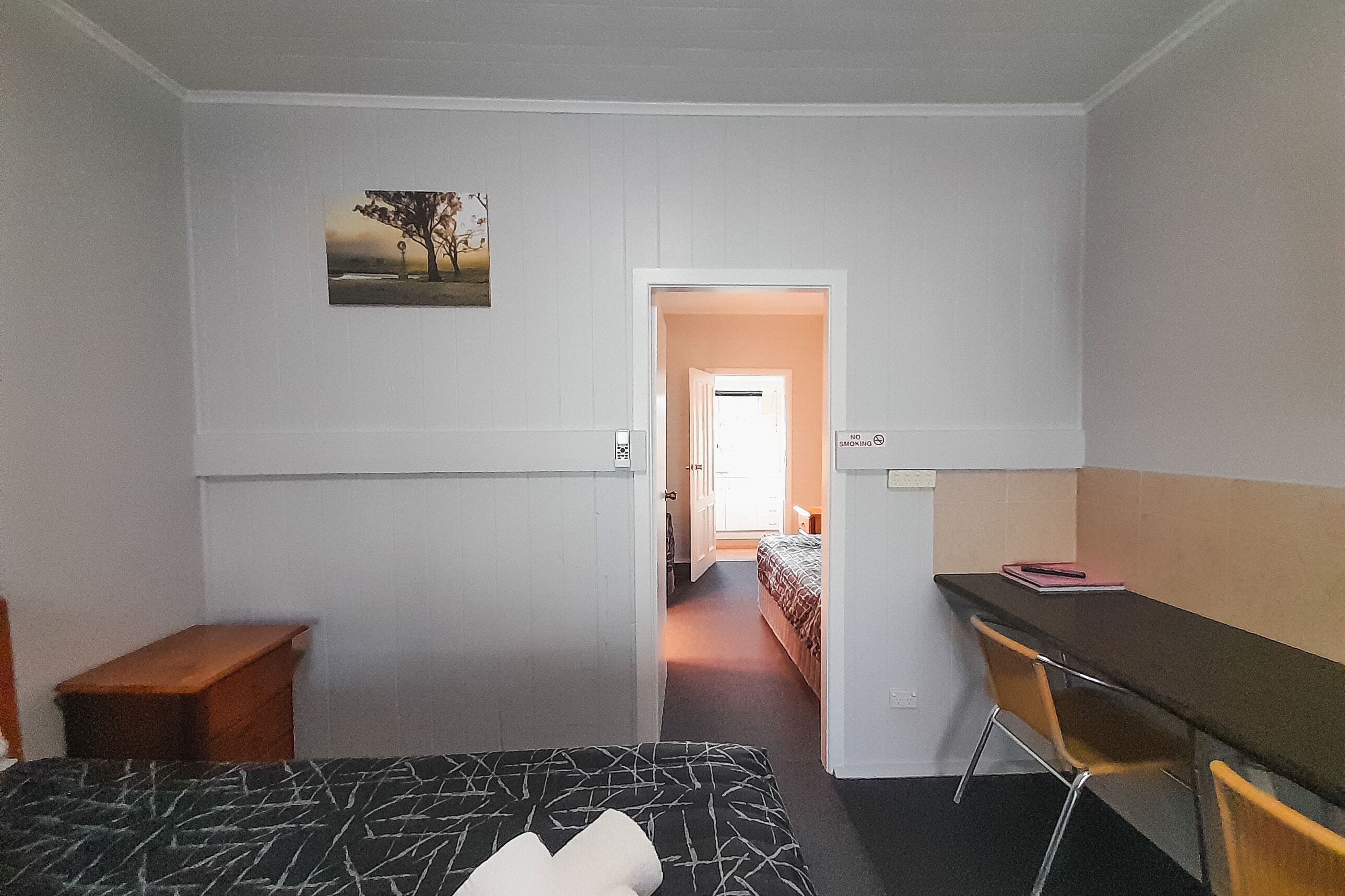 Une chambre à coucher avec un lit, un bureau, une chaise, une petite table en bois et un tableau accroché au mur.