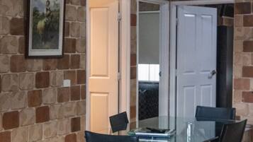A dining area with a glass table and four chairs, a framed picture on the wall, and a stone wall.