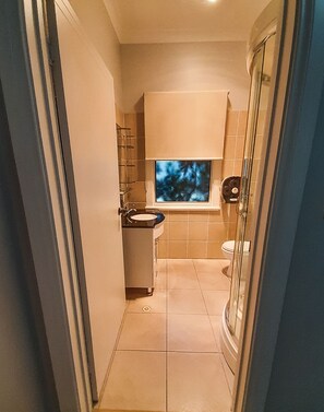 A narrow bathroom with a shower, toilet, and sink.