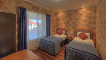 A room with two single beds, a wooden table, and a brick wall.