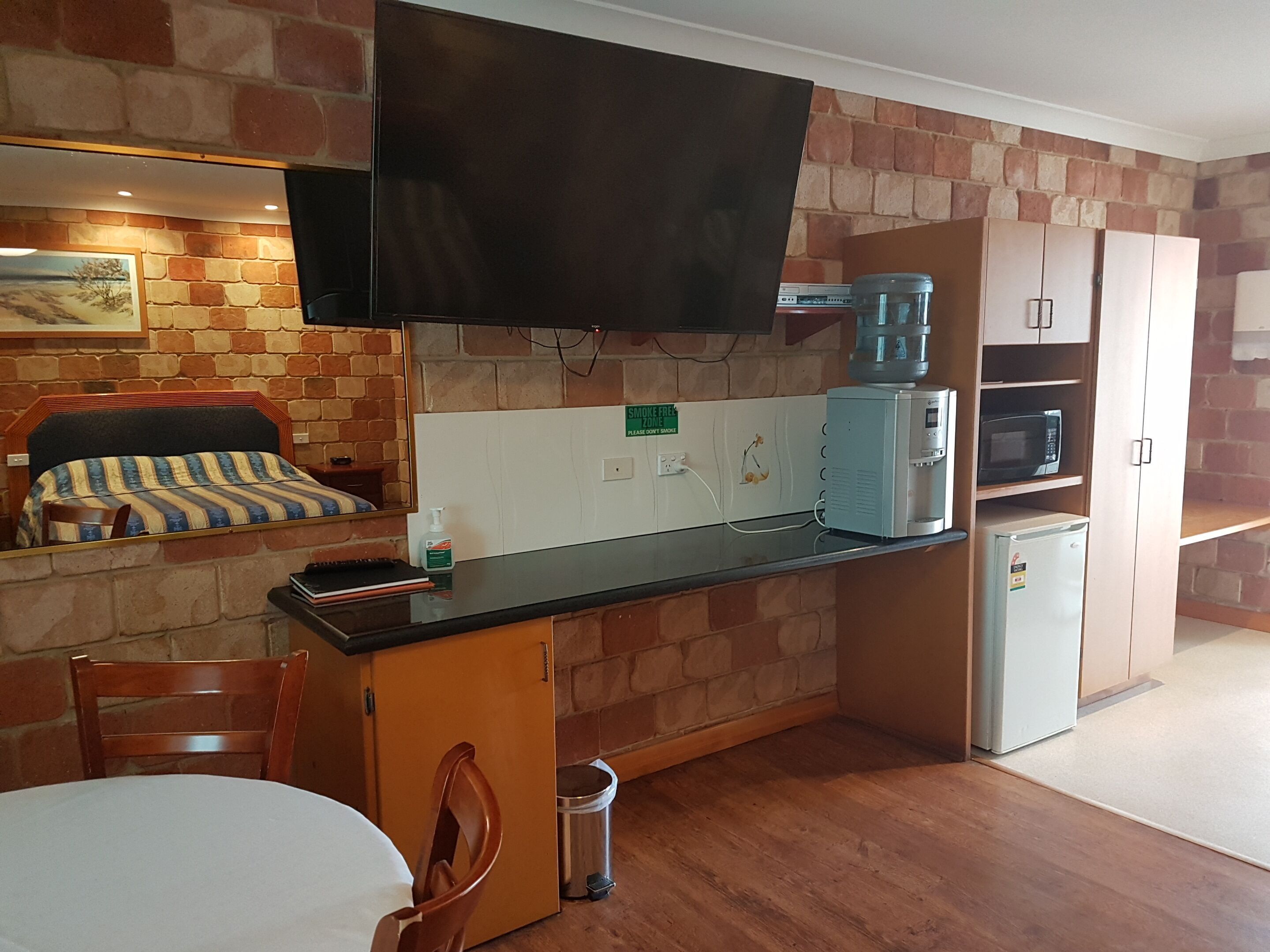 Una cocina compacta con una televisión de pantalla plana, dispensador de agua, microondas y refrigerador.
