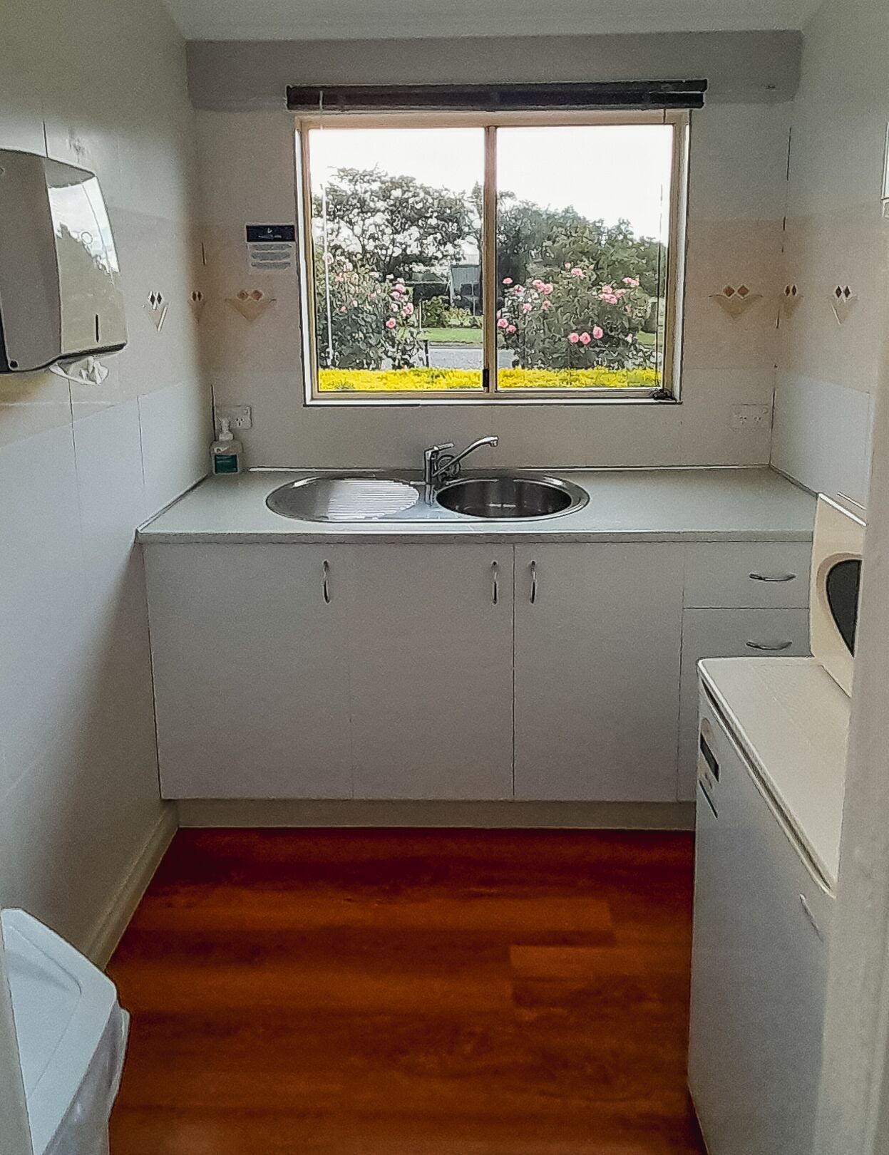 A compact kitchen with a window, white cabinets, a sink, and a microwave.