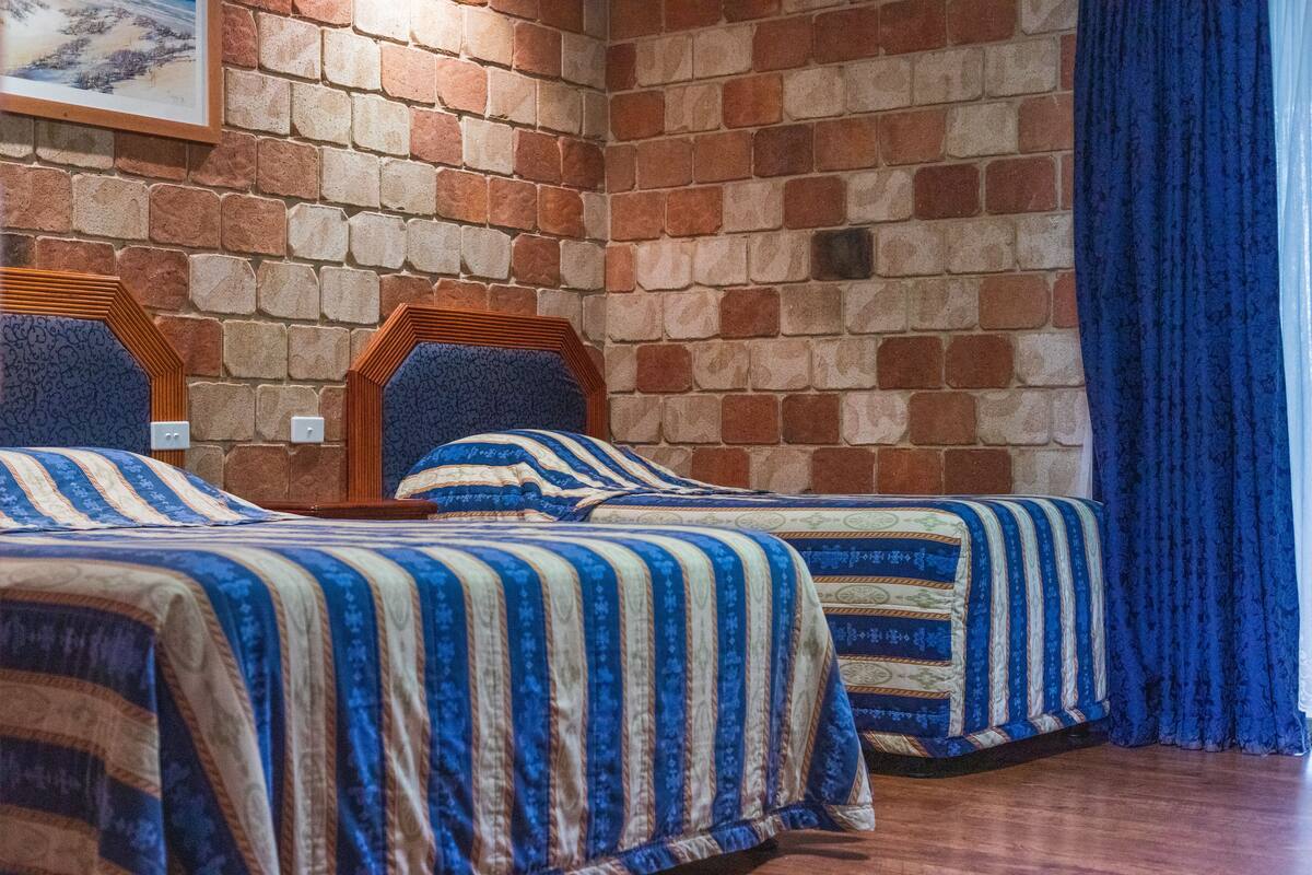 A room with two beds, a brick wall, and a blue curtain.
