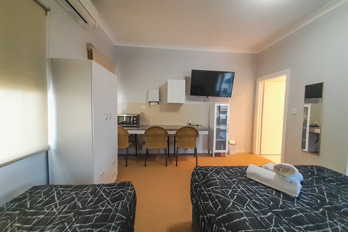 A hotel room with two beds, a small kitchenette, a TV, and a mirror.