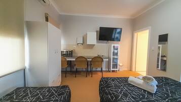 Una habitación de hotel con dos camas, una kitchenette pequeña, un televisor y un espejo.