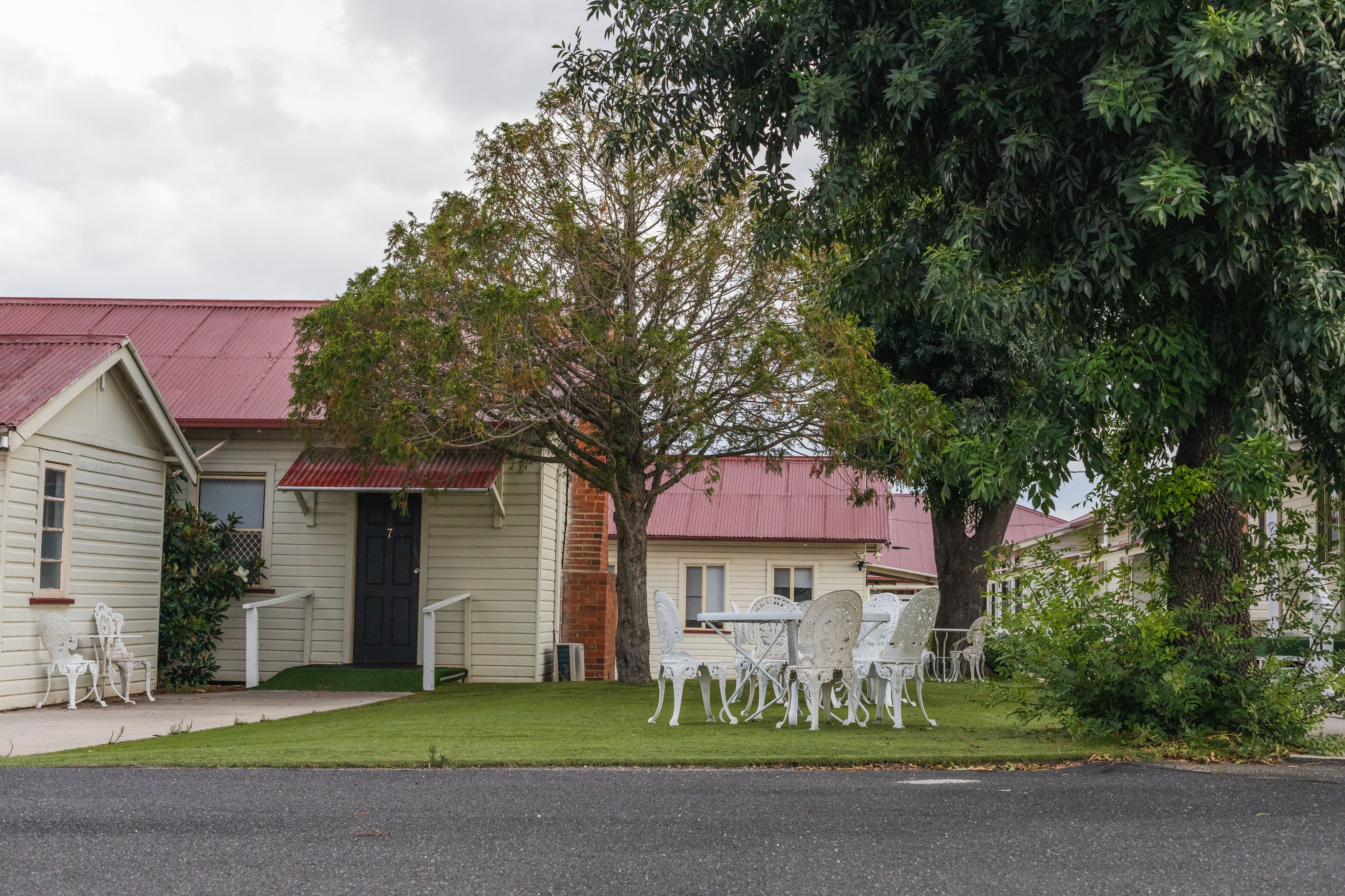 A house with a red roof, white exterior, and a lawn with white outdoor furniture.