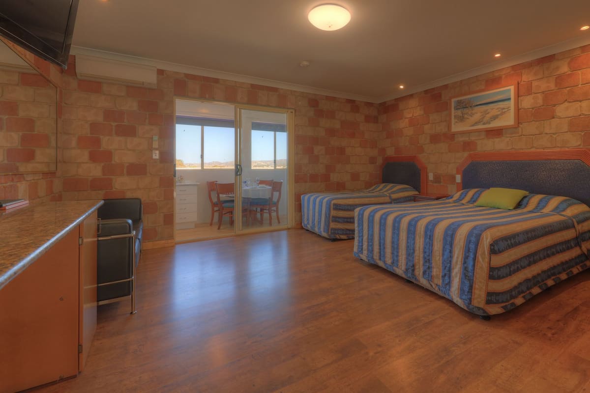 A bedroom with two beds, a desk, and a chair. There is a sliding glass door leading to a balcony.