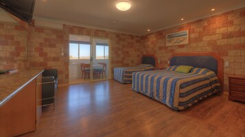 Habitación con dos camas, un escritorio y una silla. Hay una puerta corrediza de vidrio que da a un balcón.