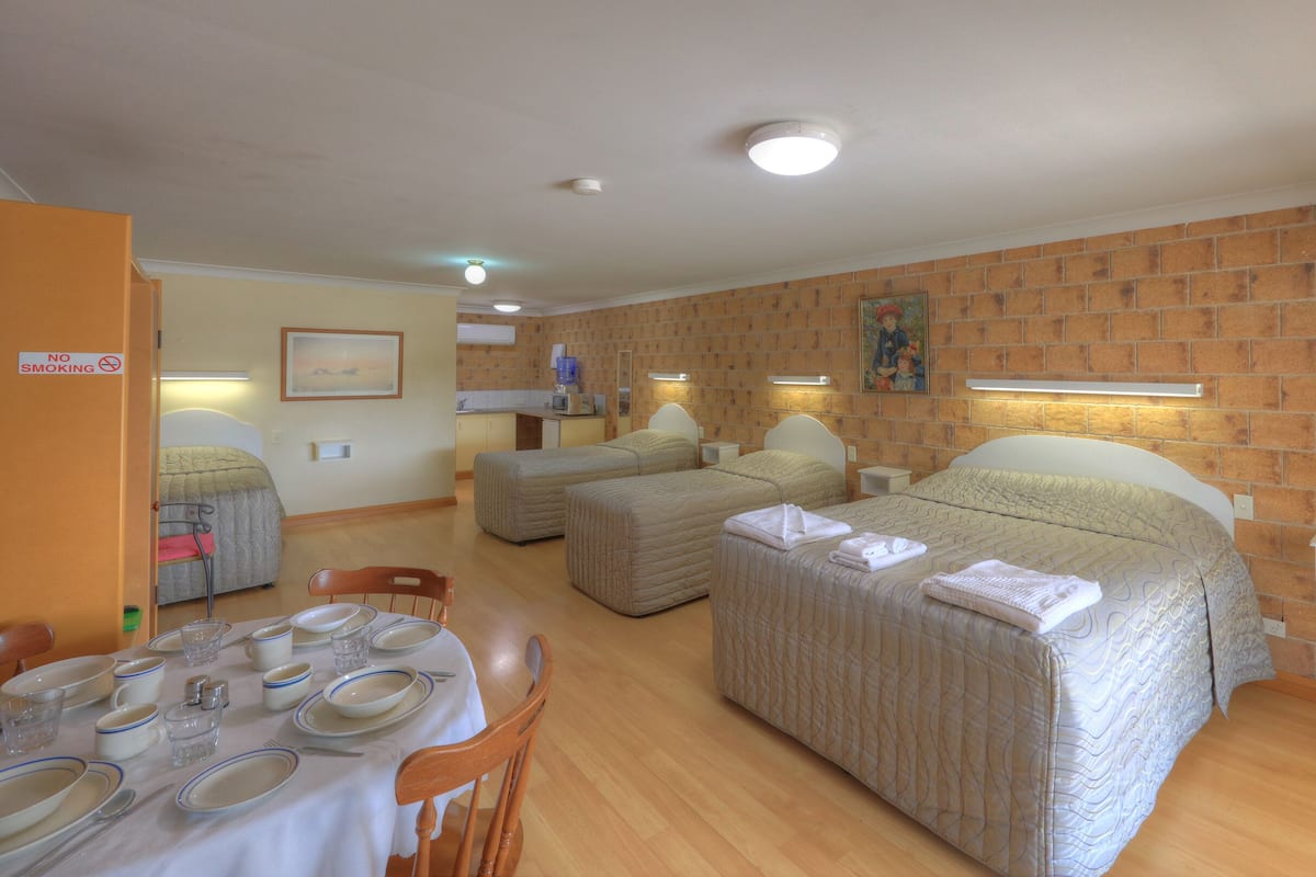 A hotel room with two beds, a dining area with a table set for four, and a kitchen area.