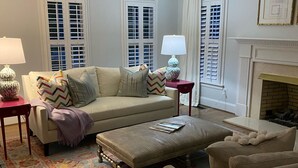 A living room with a beige sofa, patterned throw pillows, a red side table with a lamp, a patterned rug, and a fireplace. - Great Get Away Home  (Henrico)