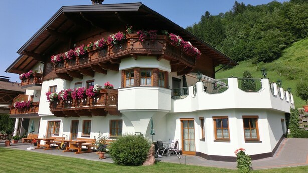 A traditional chalet with wooden balconies, flower boxes, and a patio area.