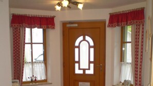 A hallway with a wooden door, a potted plant, a red carpet, and windows with red curtains.