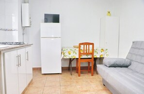 A compact kitchen with white cabinets, a built-in stove, a refrigerator, and a dining table with a lemon-patterned tablecloth. - Brezo apartment near the beach (Conil de la Frontera)