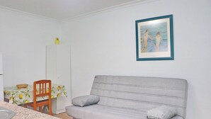 A living room with a grey sofa, a dining table with chairs, and a framed painting on the wall.