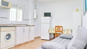 A compact kitchen with a washing machine, a refrigerator, and a dining area with a table and chair.