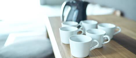 Una mesa de madera con seis tazas blancas de cerámica y una tetera eléctrica negra.