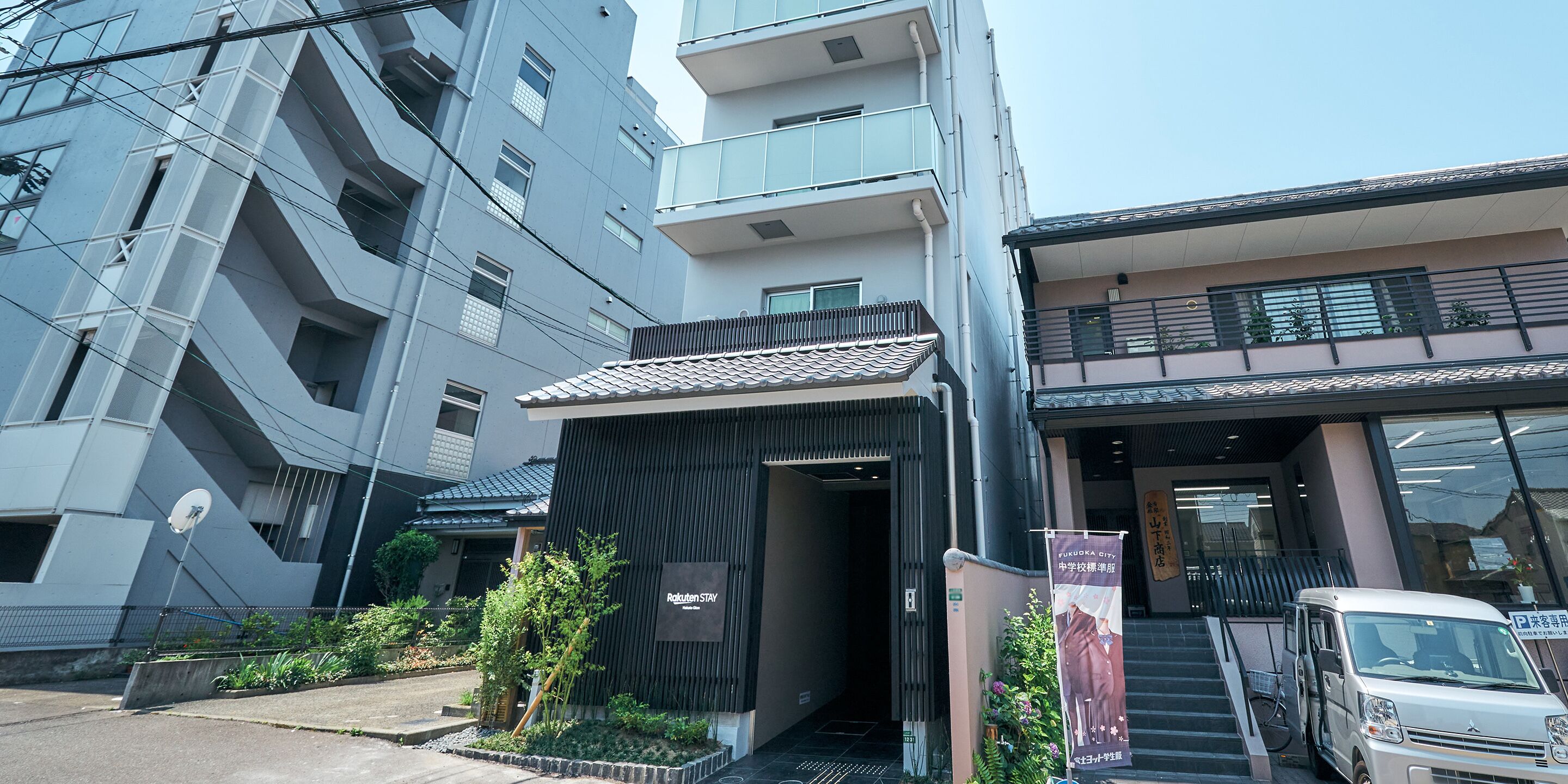 A modern building with a sign for Fukuoka City, a parking area, and a vehicle parked outside.