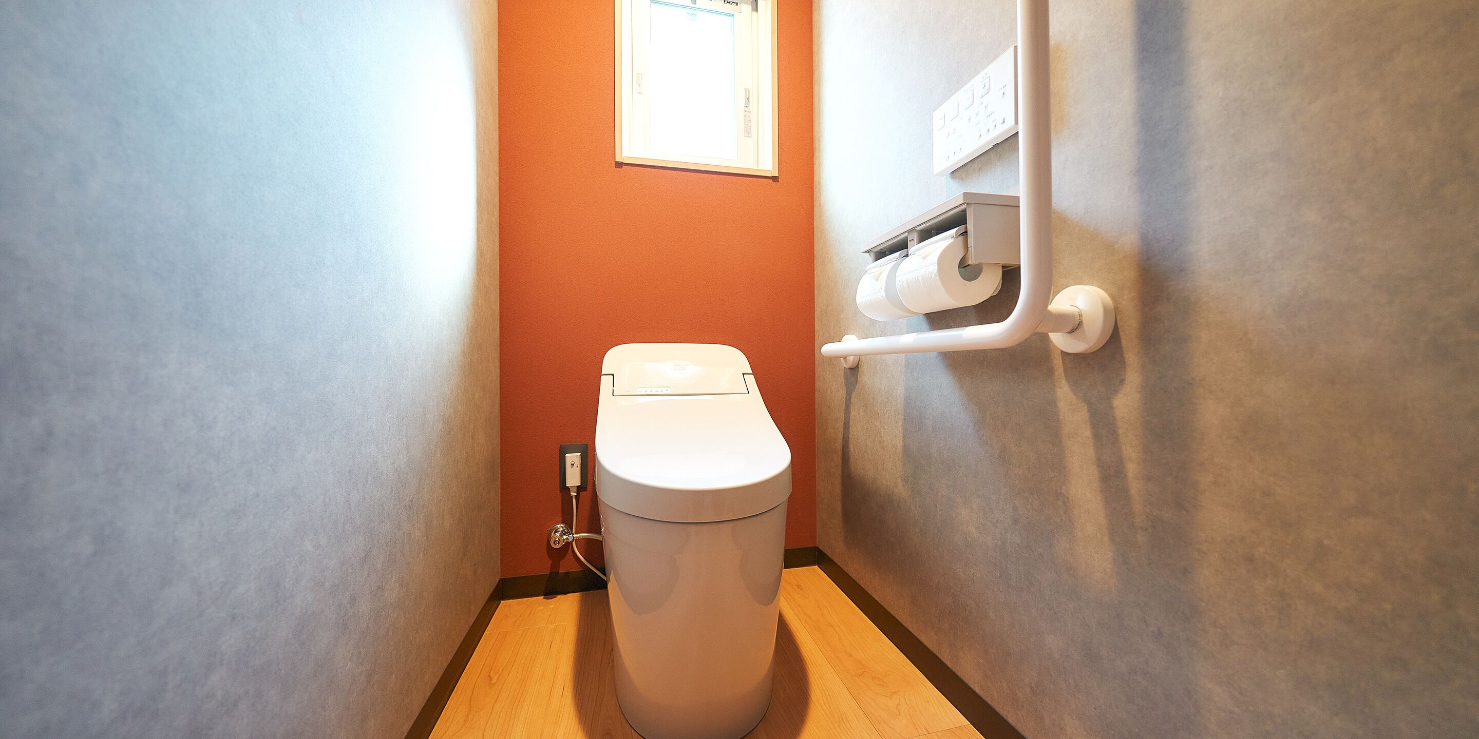 A compact bathroom with a toilet, a paper towel dispenser, and a wall-mounted electrical outlet.