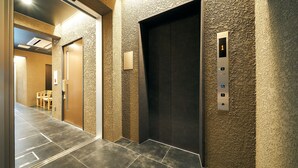 An elevator with a textured wall, a control panel, and a door. - Rakuten STAY Hakata Gion (Fukuoka)