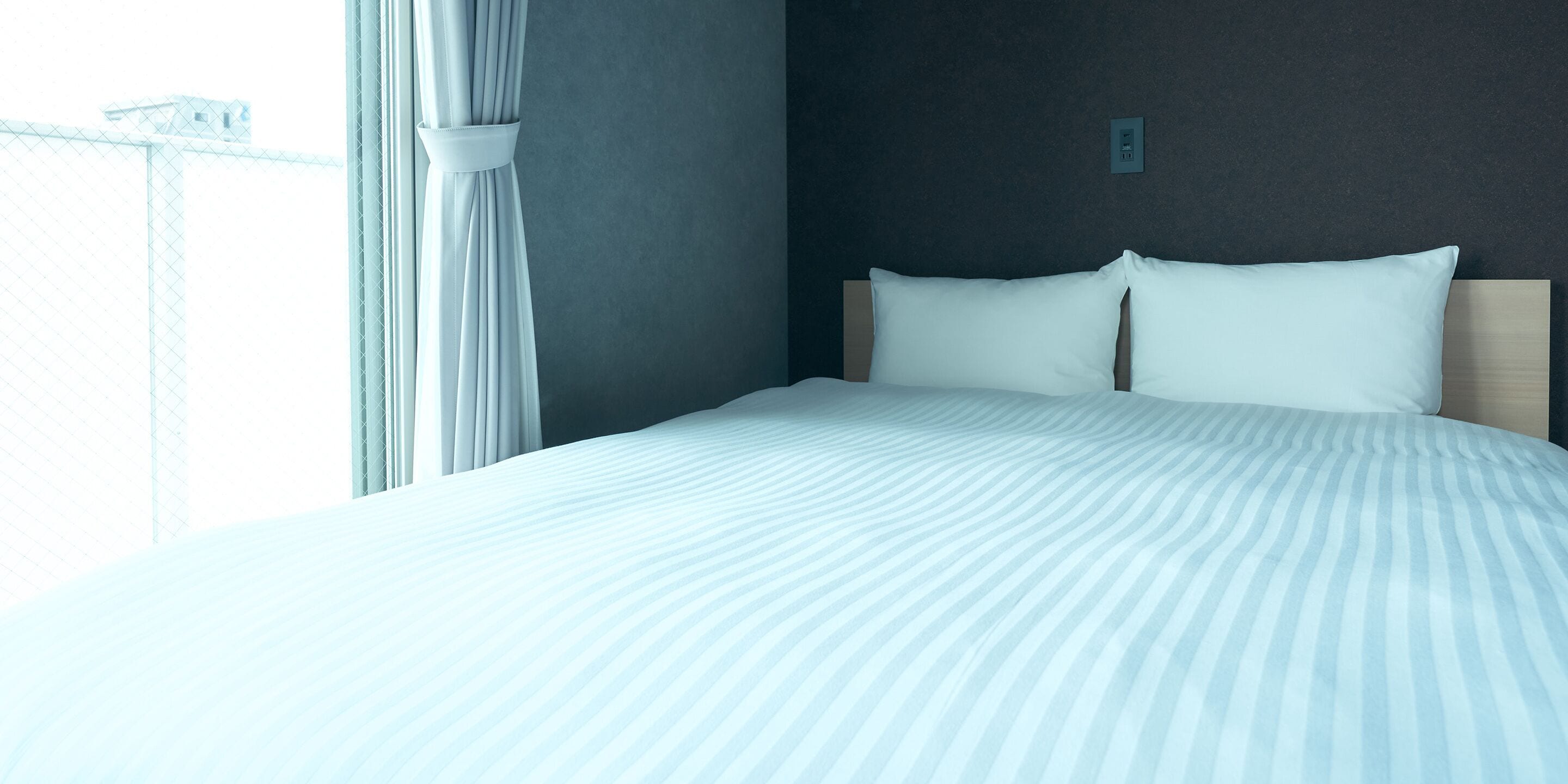 A neatly made bed with white bedding and a wooden headboard in a room with a dark wall and a window with curtains.