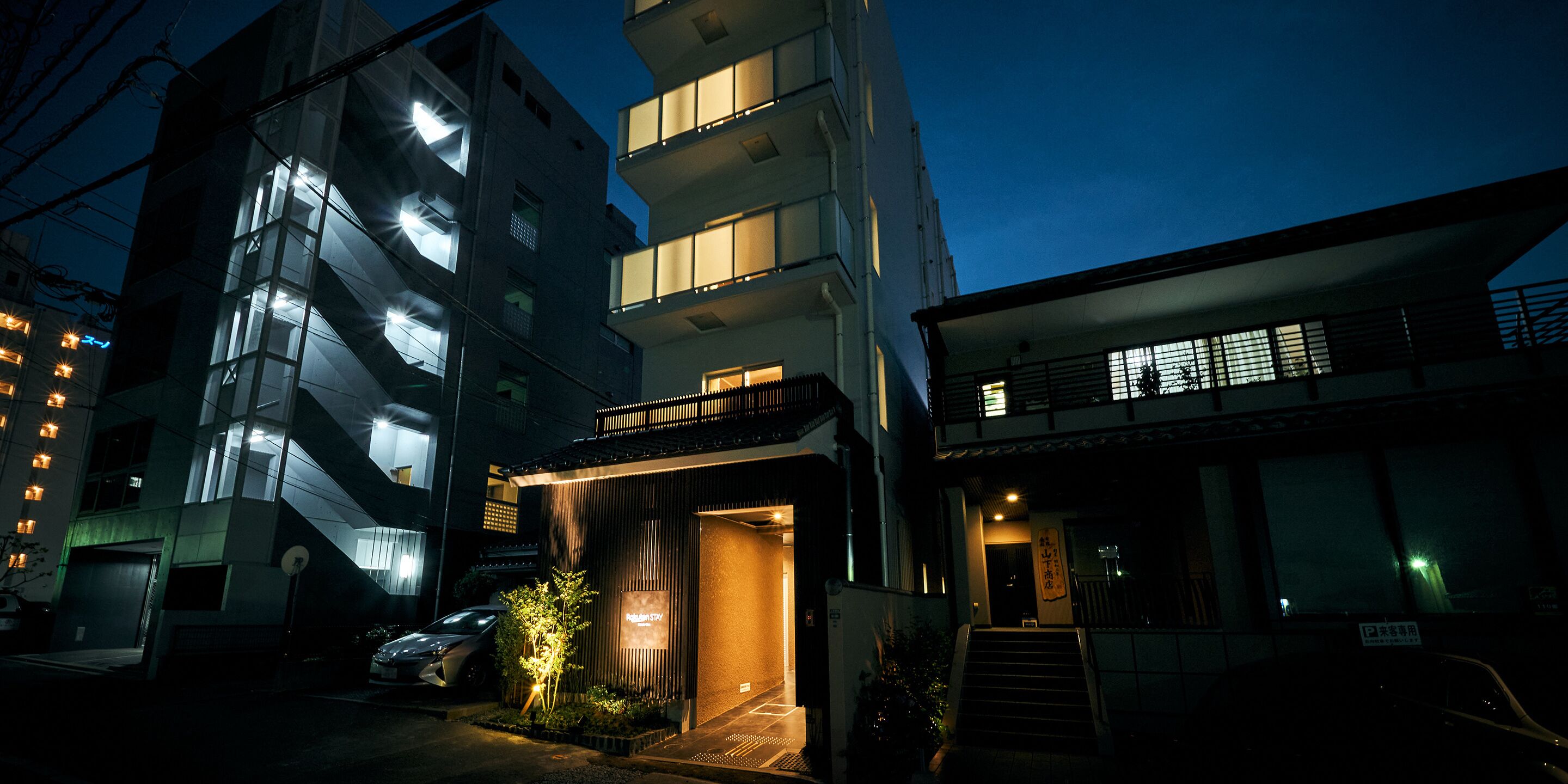 A modern building with multiple floors, a visible entrance, and a parking area.