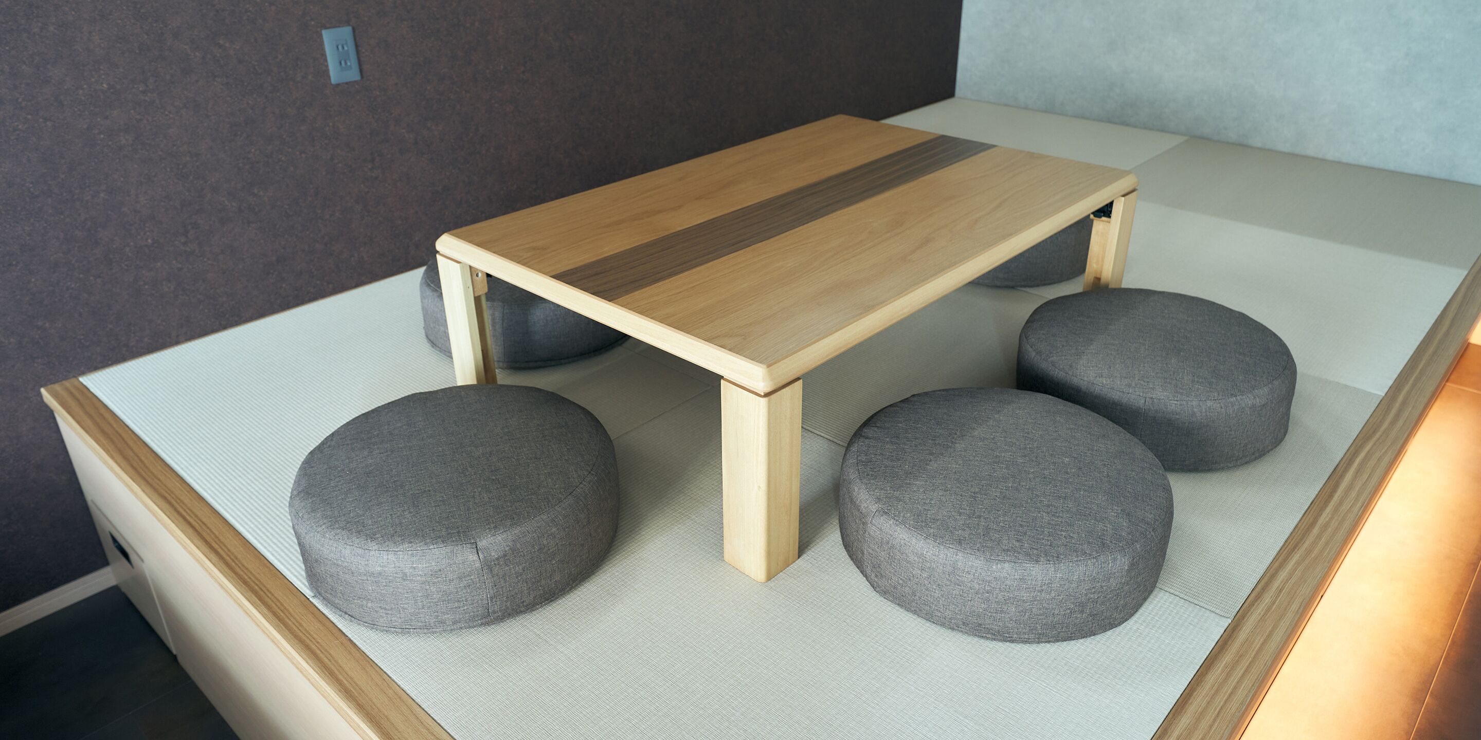 Una mesita de madera con tapa clara y cuatro cojines grises.