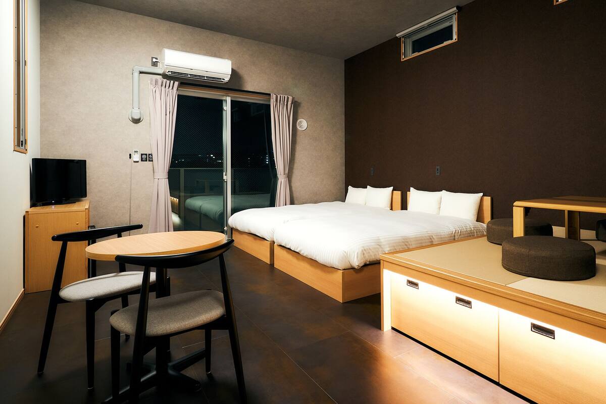 A modern hotel room with a bed, a desk, a chair, a small table, and a sofa.